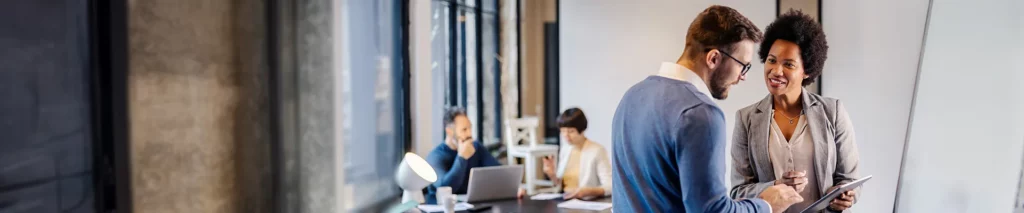 Onboarding Schulung - Gespräch zwischen zwei Personen mit weiteren Personen im Hintergrund